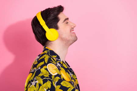 Young man enjoying music with bright headphones wearing tropical shirt against vibrant pink backgroundの写真素材