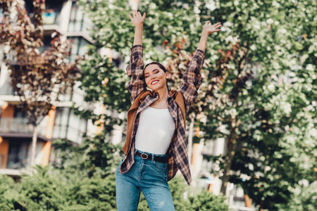 Happy Young Woman Enjoying a Relaxed Moment Outdoors in a Vibrant Urban Setting Surrounded by Lush Green Foliageの写真素材