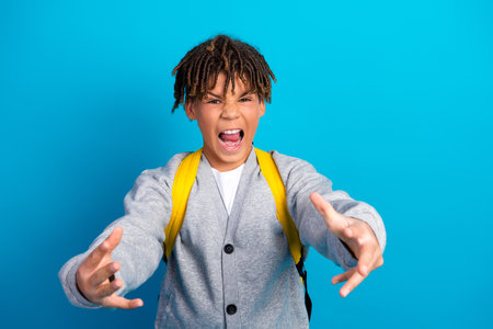 Lively schoolboy expressing excitement with dynamic hand gestures against a vibrant blue background wearing casual school uniformの写真素材