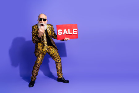 Eccentric elderly man holding sale sign in stylish outfit on bright purple background showcasing a lively and vibrant shopping promotionの写真素材