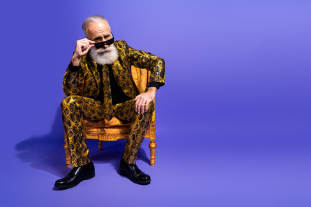 Confident elderly gentleman in an extravagant printed suit posing stylishly on a purple background showcasing charisma and eleganceの写真素材