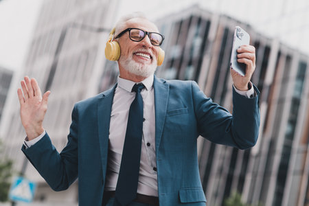 Confident senior businessman enjoying music outdoors while celebrating success in his professional careerの写真素材