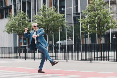 Confident businessman in a blue suit walking enthusiastically on a city street feeling successful during a sunny dayの写真素材