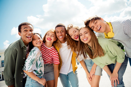 Multicultural group of cheerful young adults laughing together outdoors on a sunny day, fostering...