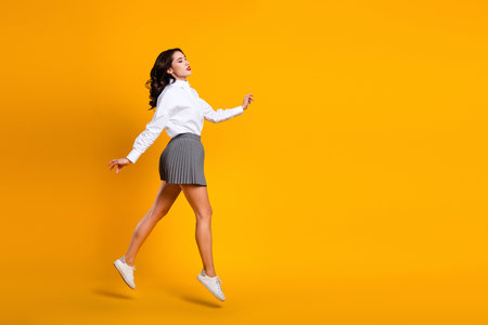 Charming stylish woman in a white shirt and gray skirt confidently walking against a vibrant yellow...