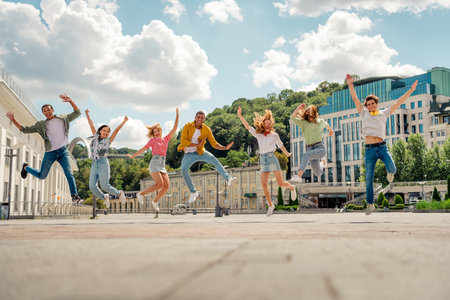 Group of diverse young adults jumping together joyfully in an urban setting, embracing friendship...