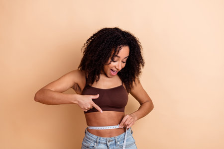 Joyful woman measuring her waistline and showcasing a healthy lifestyle on a beige backgroundの写真素材