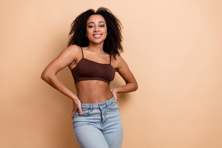 Attractive young woman posing confidently in stylish casual fashion in front of a beige background, smilingの写真素材
