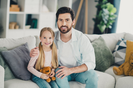 Young father and daughter bonding on a cozy couch indoors with cheerful smiles and enjoying quality...