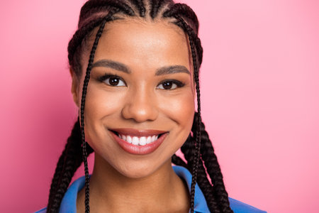 Close-up of a cheerful young woman with braids, smiling against a bright pink backdrop, expressing...