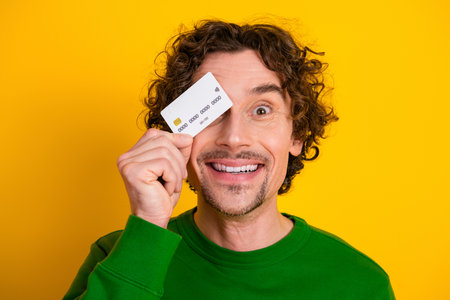 Happy man holding a credit card peeking through it against a bright yellow background, emphasizing modern lifestyleの写真素材