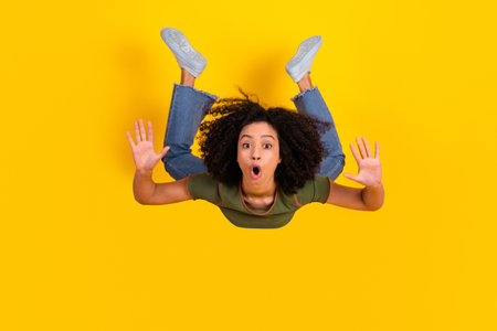 Cheerful young woman looking surprised in green t-shirt and jeans against bright yellow background