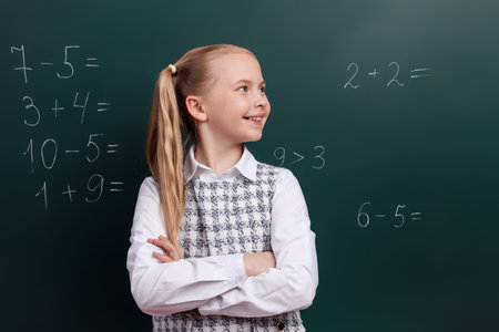 Smiling schoolgirl in classroom, standing confidently against chalkboard with math equations