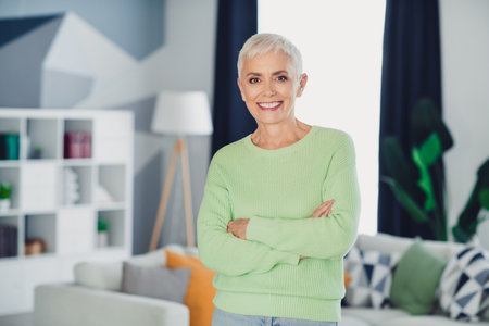 Charming mature woman with short white hair in casual sweater at home, smiling confidently in a cozy...