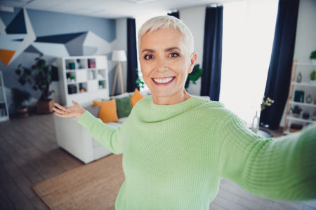 Happy mature woman in bright green sweater enjoying a moment in her stylishly decorated home with modern decorの写真素材