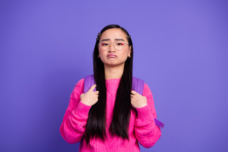 Young stylish woman with long dark hair in a pink sweater and glasses standing in front of a vibrant...