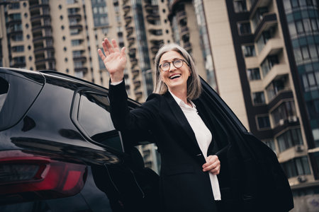 Confident elegant senior businesswoman smiling while exiting a car against an urban cityscape background during daylightの写真素材