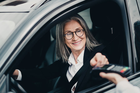 Elegant mature businesswoman in formalwear making a contactless payment while seated in a car during...