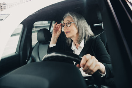 Confident mature businesswoman in formal suit driving a car in an urban setting, representing success and professionalismの写真素材