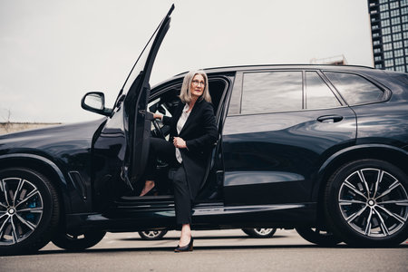Successful mature businesswoman stepping out of an elegant car in an urban setting on a daytime outdoor engagementの写真素材