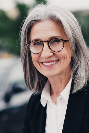 Elegant mature businesswoman outdoors wearing formalwear with glasses, showcasing elegance and success, urban backgroundの写真素材