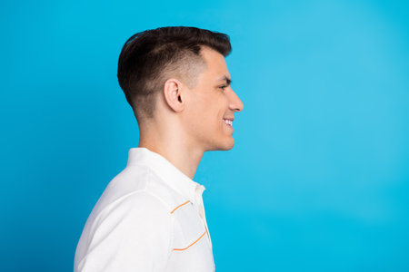 Side profile of a smiling man in a white shirt against a bright blue background expressing positivity and confidenceの写真素材