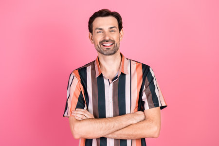 Portrait of a cheerful young man in a striped shirt on a vibrant pink background with crossed arms looking confidentの写真素材