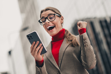 Excited young professional reacting to good news outdoors in downtown wearing stylish checkered jacketの写真素材