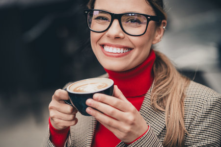 Confident young businesswoman enjoying a latte outdoors in a stylish outfit, radiating charm and professionalismの写真素材