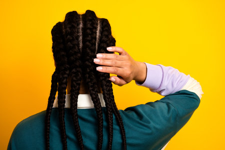 Close-up portrait of a woman with braided hair resting her hand on her head against a bright yellow backgroundの写真素材