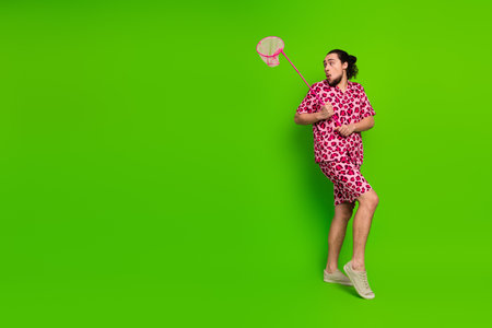 Young man in pink leopard print outfit posing against bright green background holding playful prop, conveying humor and energyの写真素材