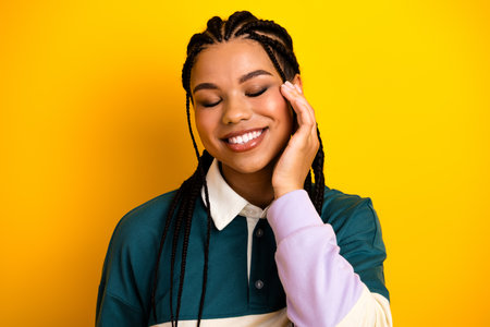 Joyful young woman with braids posing against vibrant yellow background with hand gesture in a...