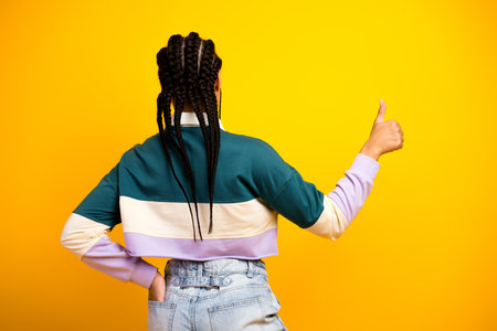 Young woman in casual attire gesturing confidently against a vibrant yellow background with braided hairstyleの写真素材