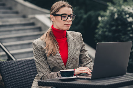 Professional businesswoman working outdoors on a laptop in an urban setting with focus and determinationの写真素材