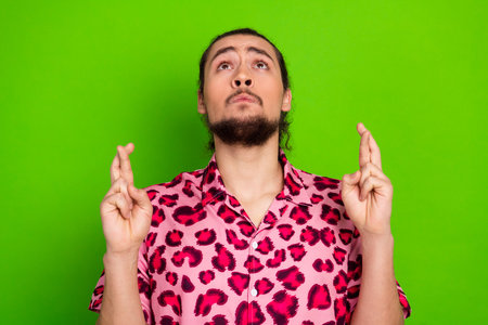 Young man in a stylish pink leopard print shirt crossing fingers on both hands against a bright green backdropの写真素材