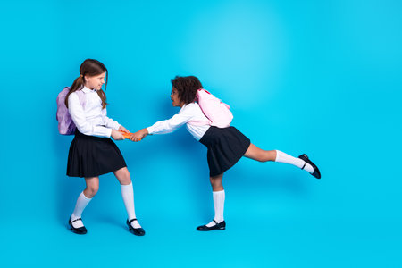 Two young schoolgirls playfully interacting on a bright blue background, symbolizing friendship, education, and youthful funの写真素材