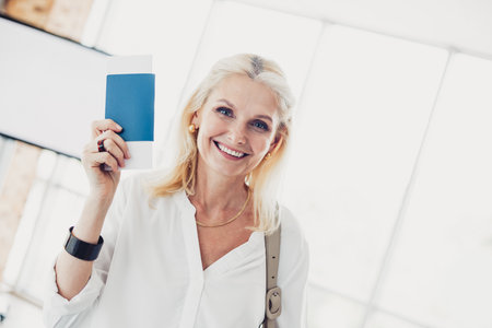 Stylish mature woman at airport with boarding pass, ready for exciting travel opportunity in a vibrant and urban summer settingの写真素材