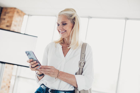 Content senior woman enjoying mobile phone connectivity in a bright airport terminal during travel...