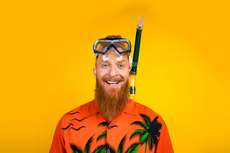 Cheerful man with snorkel and tropical shirt against yellow background exuding a joyful holiday and summer vibeの写真素材