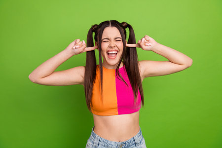 Bright young woman with a cheerful pose against a green background, expressing playful emotions in...