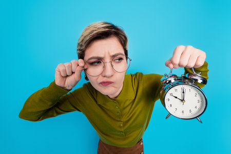 Young female professional holding an alarm clock with an expression of curiosity, wearing casual...