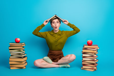Young woman with short hair sits casually surrounded by colorful book on a vibrant blue background,...