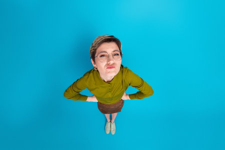 Playful young woman in stylish green top on blue background striking a quirky pose, high top viewの写真素材