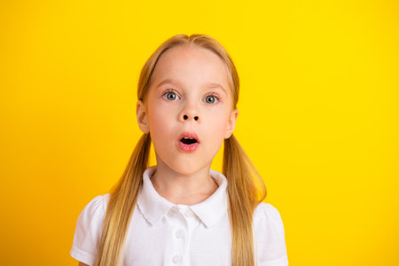 Excited young schoolgirl on a yellow background expressing surprise wearing casual white t-shirt