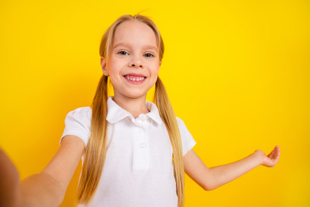 Smiling schoolgirl in white t-shirt posing with cheerful expression against vibrant yellow...