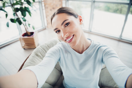 Young woman smiling brightly in a comfortable modern home setting with natural lighting and cozy interior designの写真素材