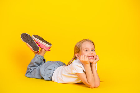 Cheerful young girl resting on a yellow background wearing casual attire and jeans with a radiant smile capturing happinessの写真素材