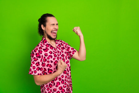 Excited young man in a leopart print pink shirt celebrating with joyful gestures on a vibrant green backgroundの写真素材