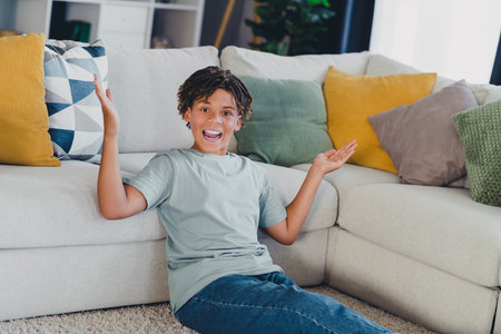 Cheerful young boy sitting casually in a cozy living room, surrounded by comfy pillows, showcasing a happy and playful mood.の写真素材