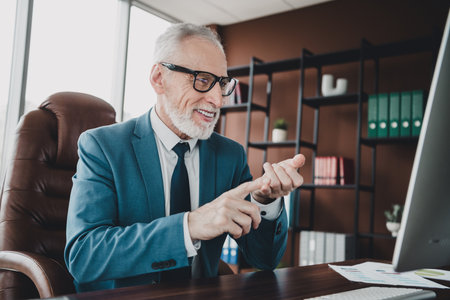 Mature businessman in formal suit working at office desk focusing on computer screen in a professional workspaceの写真素材